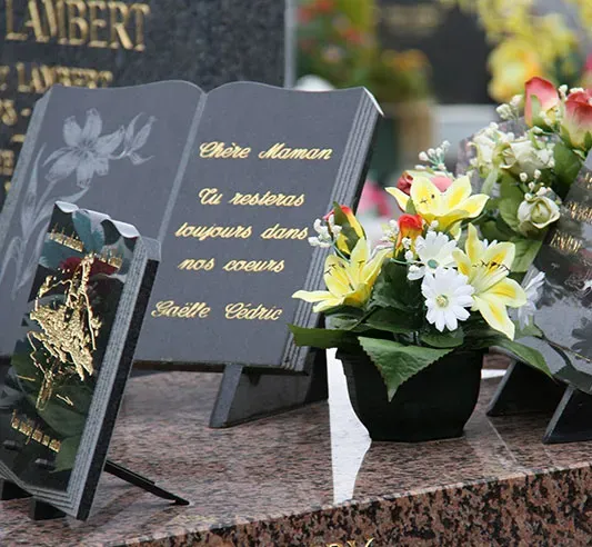 Plaques commémoratives personnalisées et fleurs artificielles sur une pierre tombale.